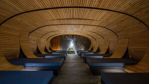 Een tunnelachtige ruimte met houten latten in het plafond en bankjes langs de wanden.
