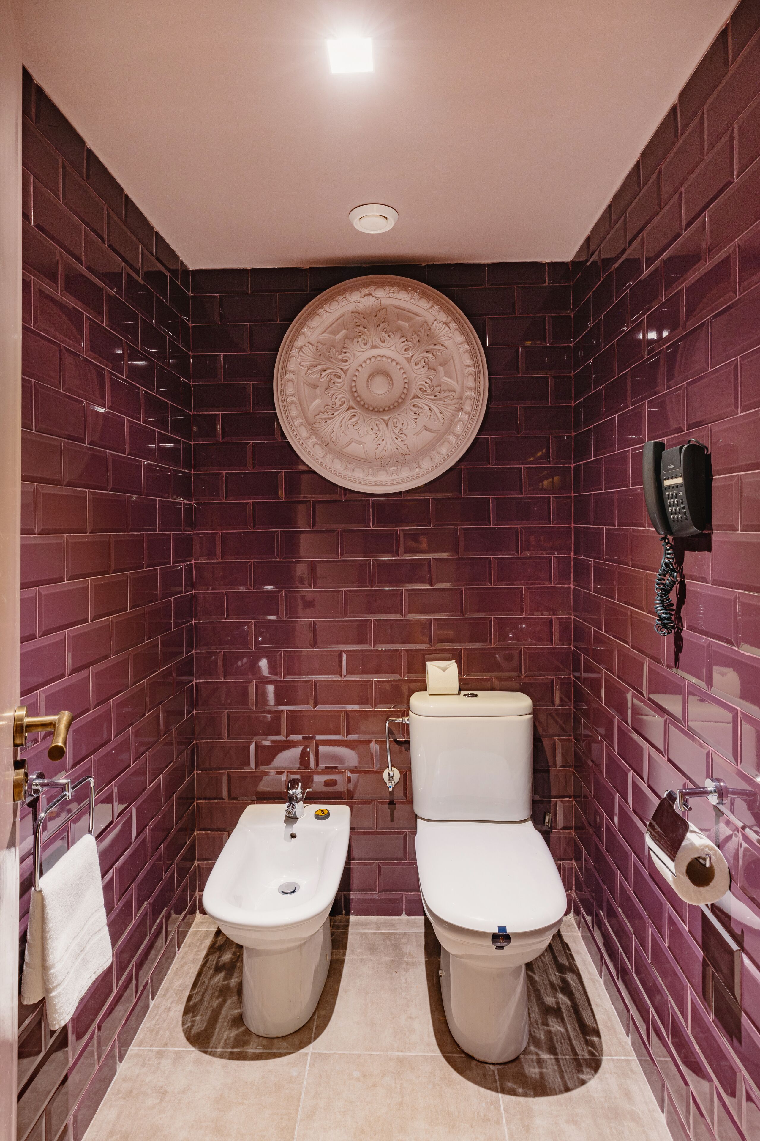 A bathroom with two toilets, a bidet, a sink, a decorative wall plate, and a telephone.