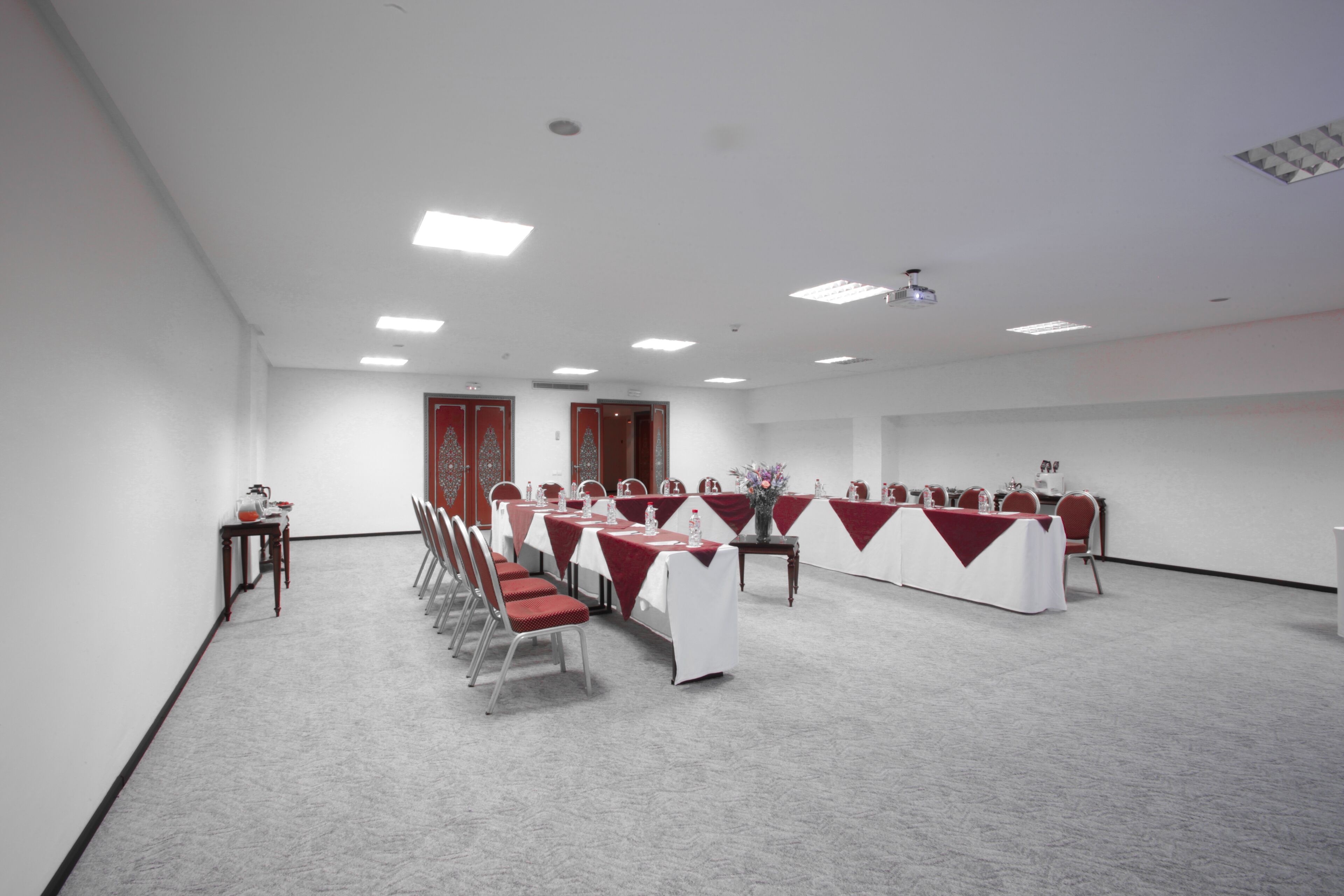 A conference room with white walls, red chairs, and tables covered with white tablecloths and red runners.