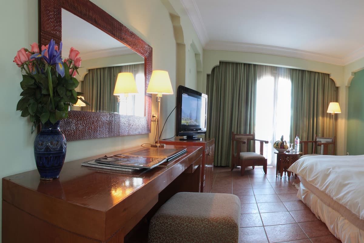 A hotel room with a bed, a desk with a laptop, a television, and a vase of flowers.