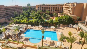 Zona de piscina de hotel con una gran piscina, tumbonas y palmeras.