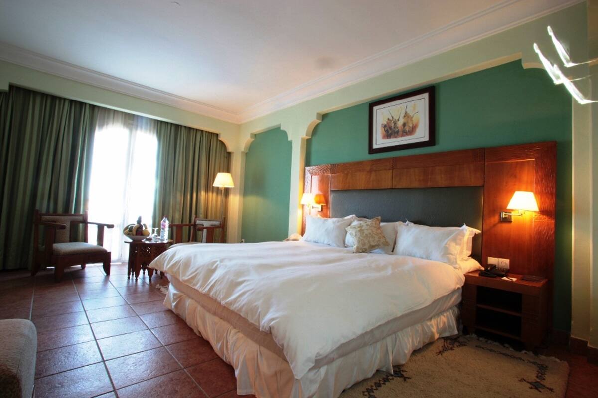 A hotel room with a large bed, two bedside tables, a chair, and a window with curtains.