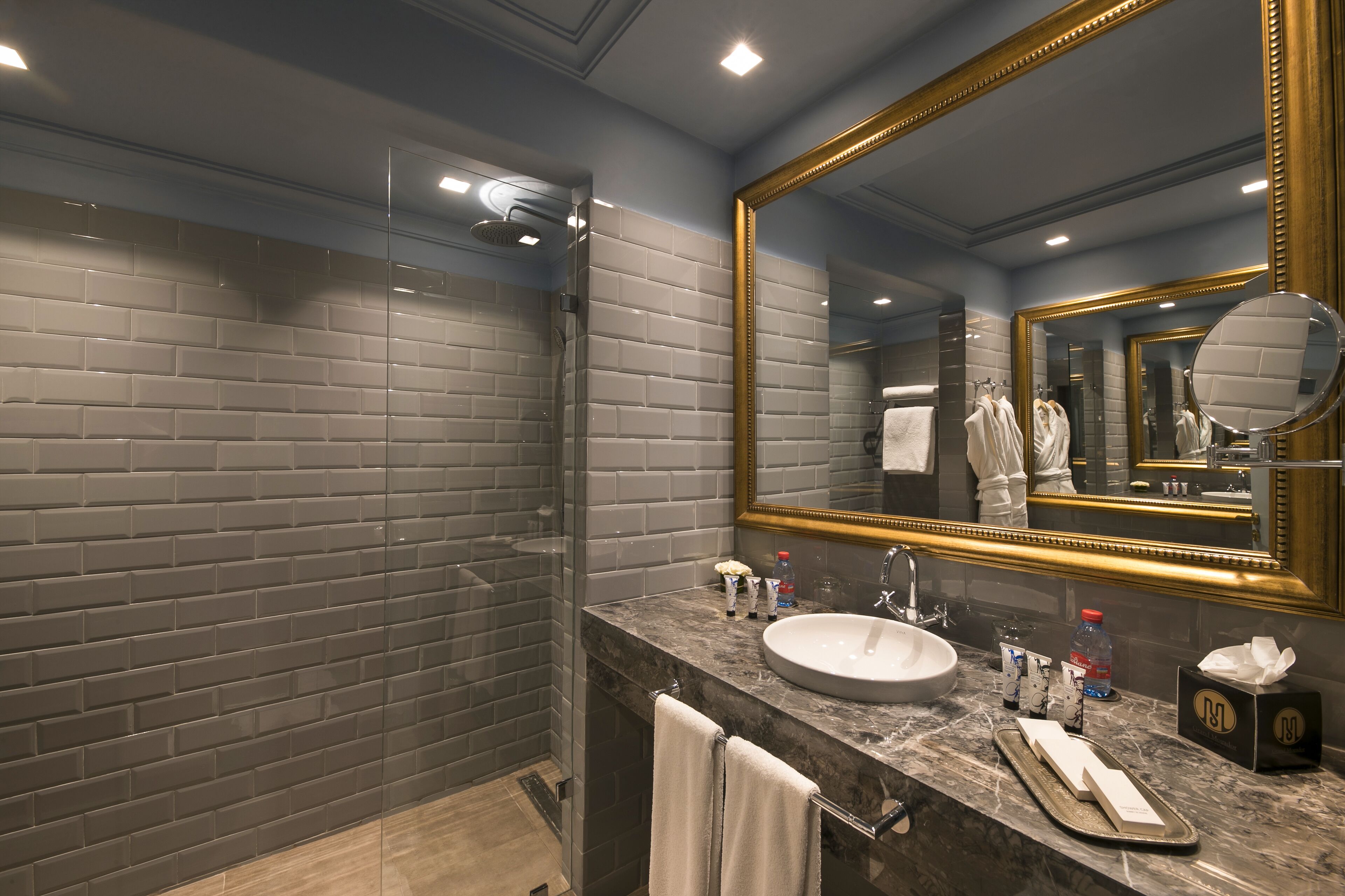 A modern bathroom with a large mirror, a glass shower enclosure, and a marble countertop with toiletries.