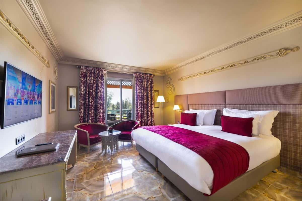 A hotel room with a large bed, a desk with a laptop, a chair, and a TV on the wall.