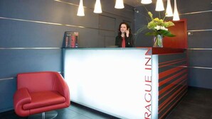 Een receptiegedeelte met een modern design, met een rode stoel, een receptiebalie met een digitaal scherm en een vaas met bloemen.