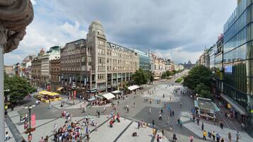 Ein belebter Platz mit historischen Gebäuden, einem zentralen offenen Bereich und einem modernen Glasgebäude auf der rechten Seite.