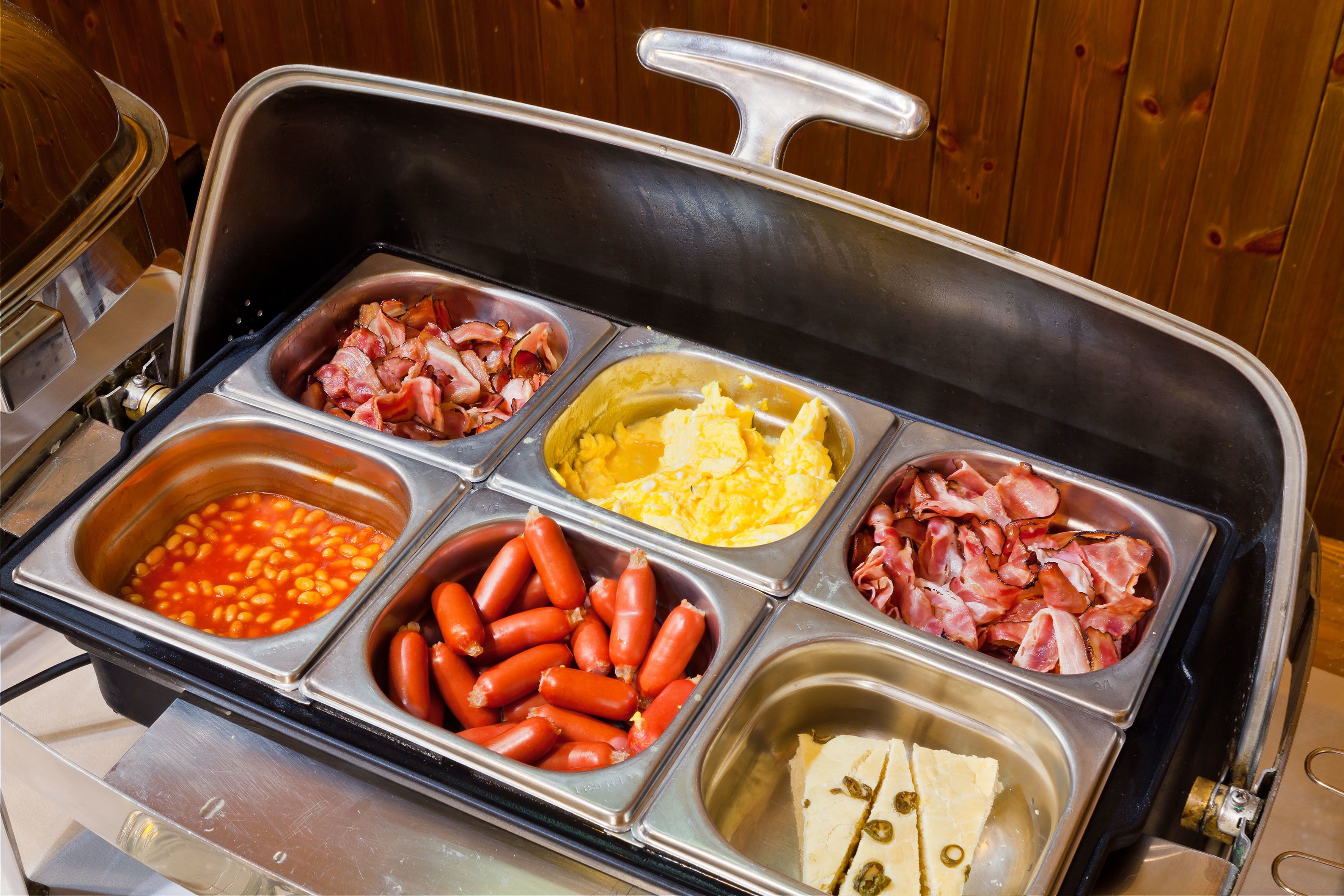 En buffet med et bredt udvalg af mad, herunder bønner, pølser, æg, bacon og ost.