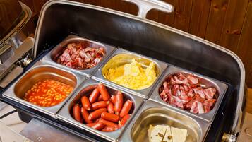 En buffet med et bredt udvalg af mad, herunder bønner, pølser, æg, bacon og ost.