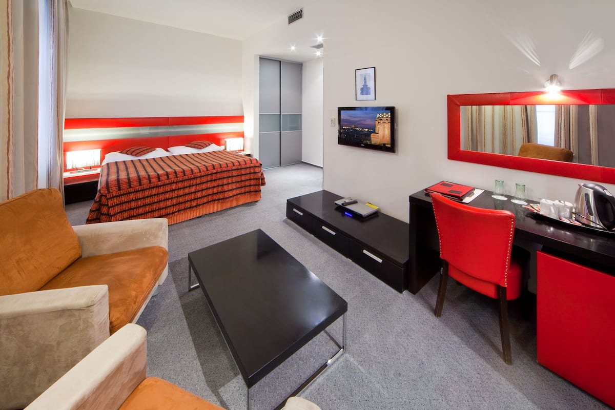 Habitación de hotel con cama, escritorio, silla, mesa de centro, televisor y espejo.