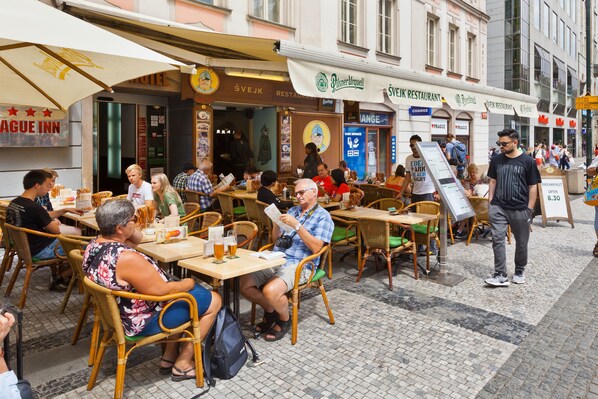 A bustling outdoor café with wicker chairs and tables, surrounded by various restaurant signs. - Hotel Prague Inn (Prague)