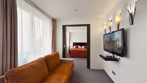 Een hotelkamer met een bank, een bed met een rood-zwarte streepdeken, een aan de muur bevestigde televisie en een raam met dunne gordijnen.