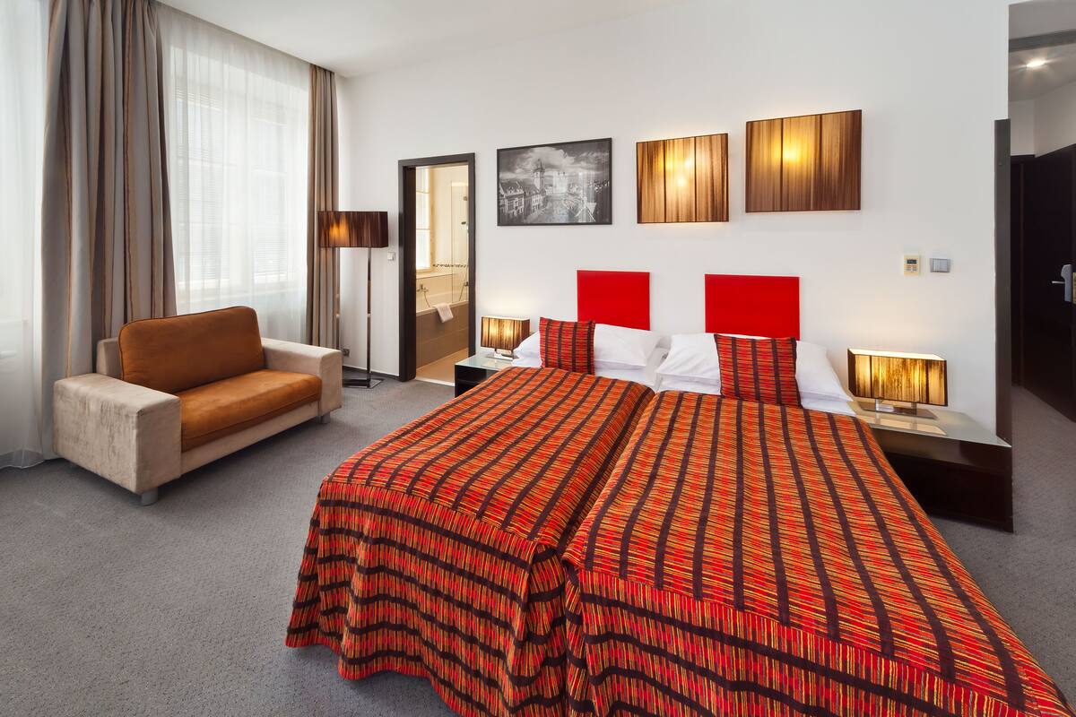 Habitación de hotel con una cama grande, un sofá, un escritorio y un baño visible a través de una puerta abierta.