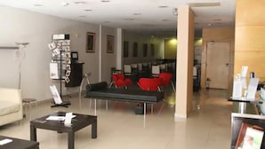 A modern lobby with a sofa, red chairs, a coffee table, a bookshelf, and a reception desk. - Argentina Tango Hotel (Buenos Aires)