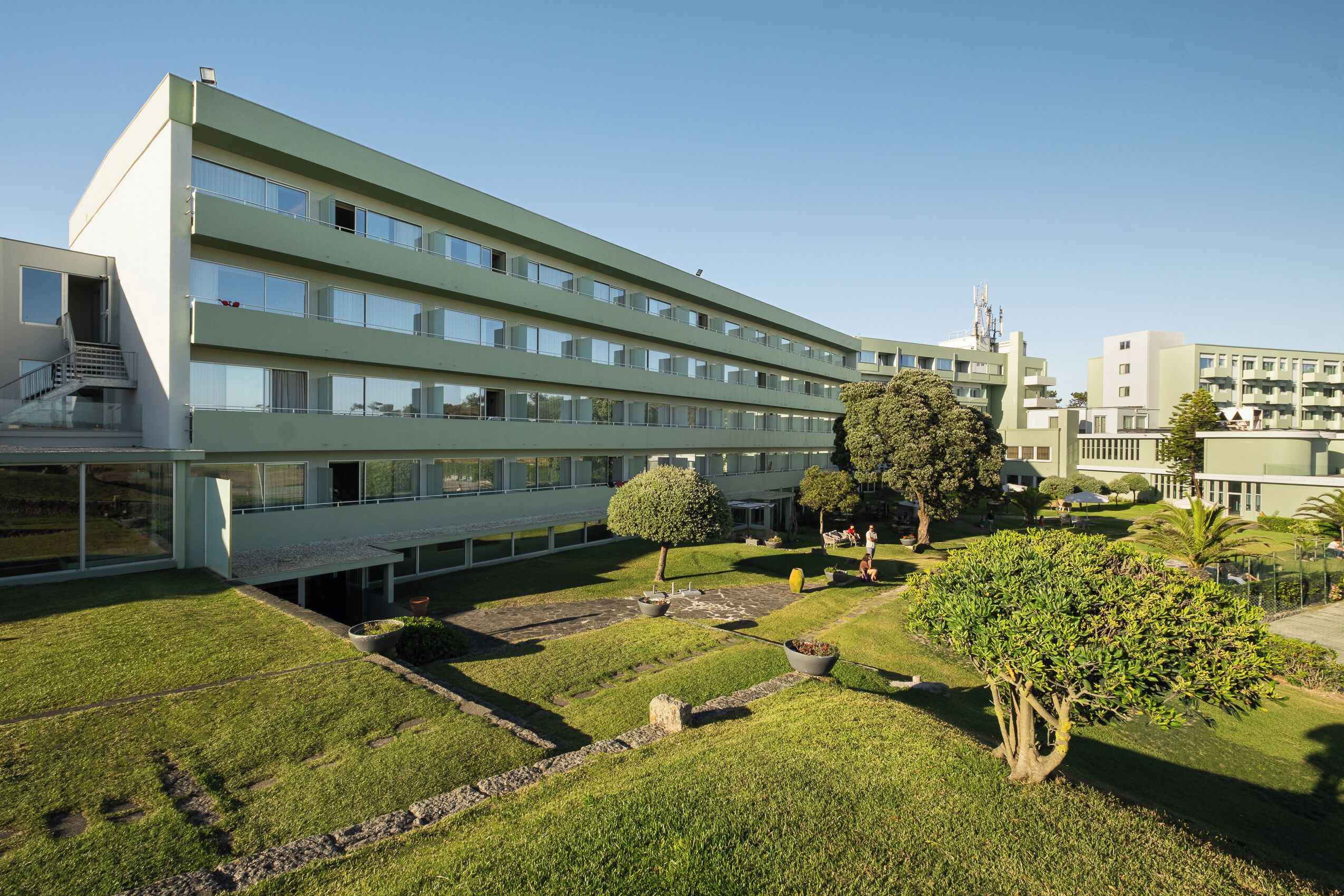 Un edificio de varios pisos con techo plano, ventanas amplias y un patio central con un árbol y una pequeña fuente.
