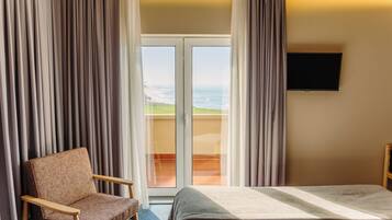 A hotel room with a bed, a chair, a TV, and a view of the ocean through a glass door.