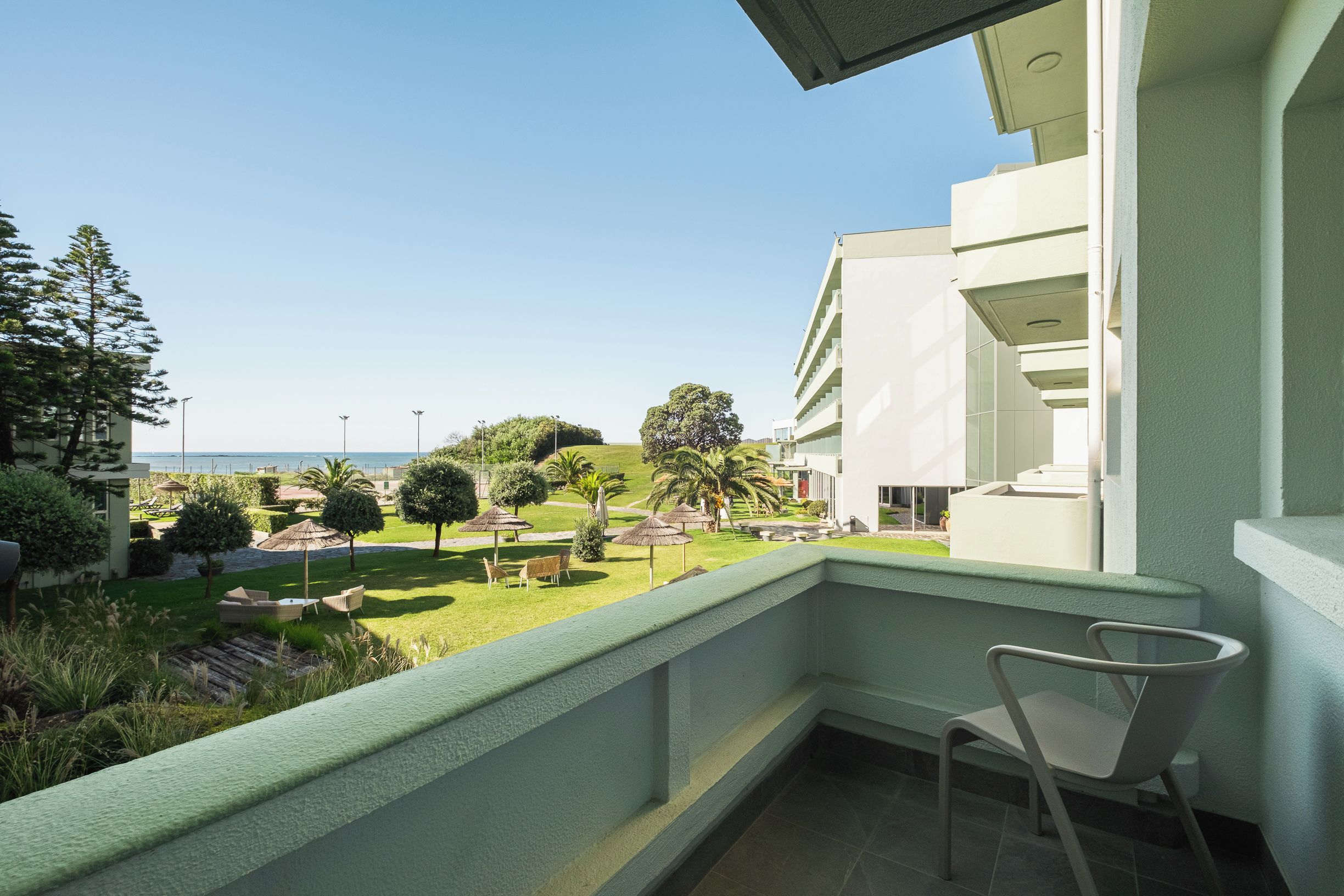 Ein Balkon mit Blick auf einen angelegten Garten und ein Gebäude im Hintergrund.
