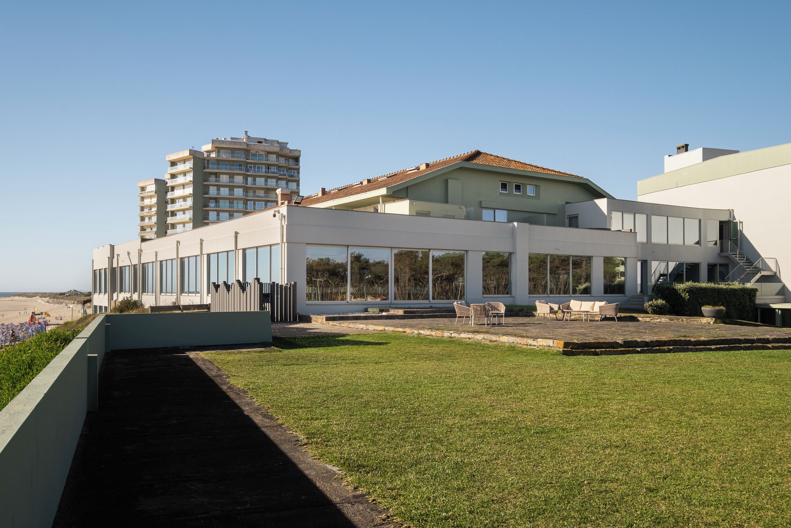 A modern building with a flat roof, large windows, and a grassy area with outdoor seating.