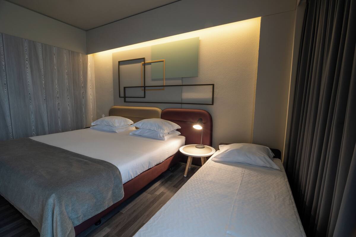 Habitación de hotel con dos camas, una mesita redonda y una lámpara fijada a la pared.