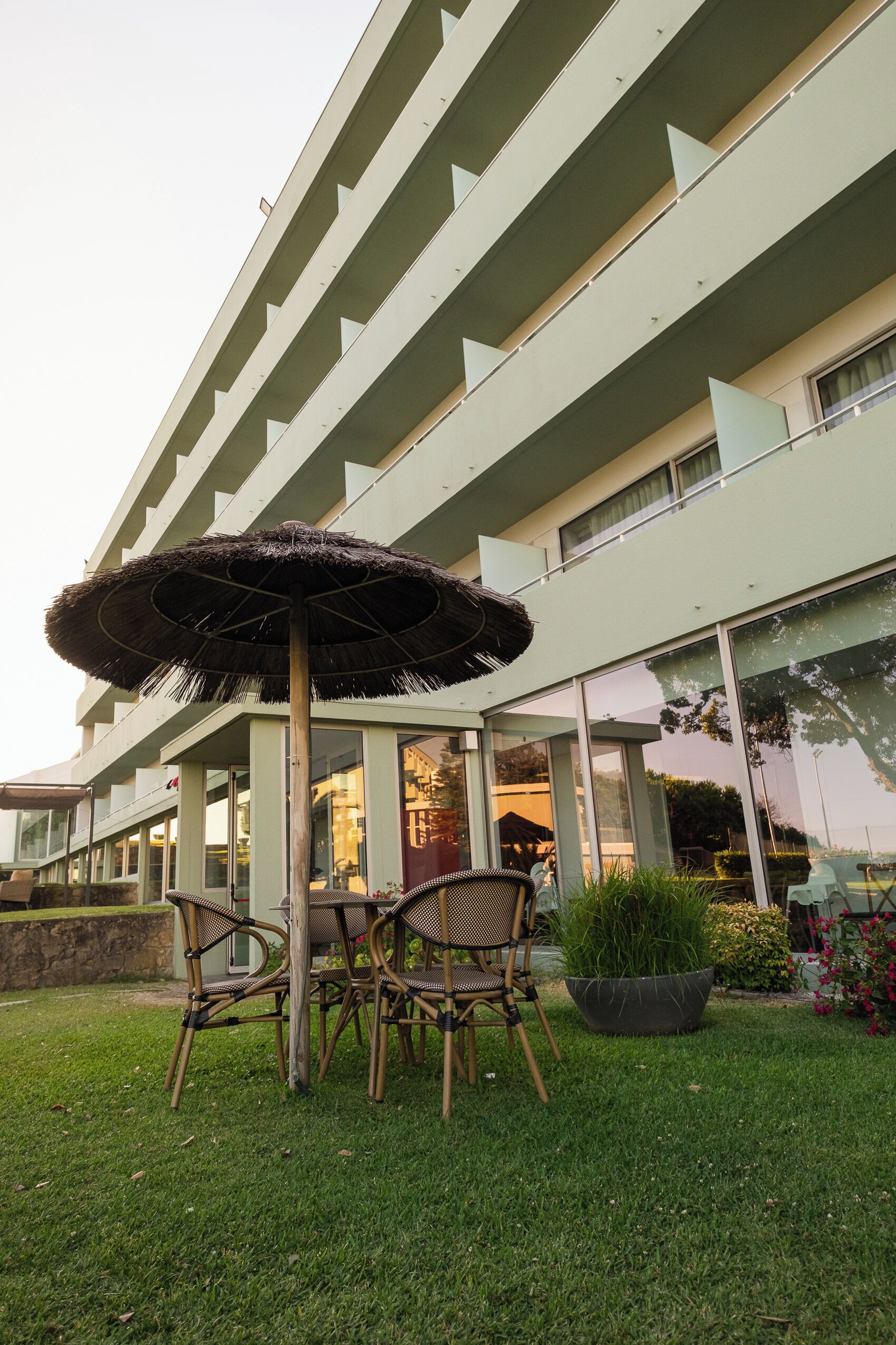 A modern building with a flat roof, large windows, and a grassy area with a table and chairs.