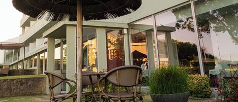 A modern building with a flat roof, large windows, and a grassy area with a table and chairs.