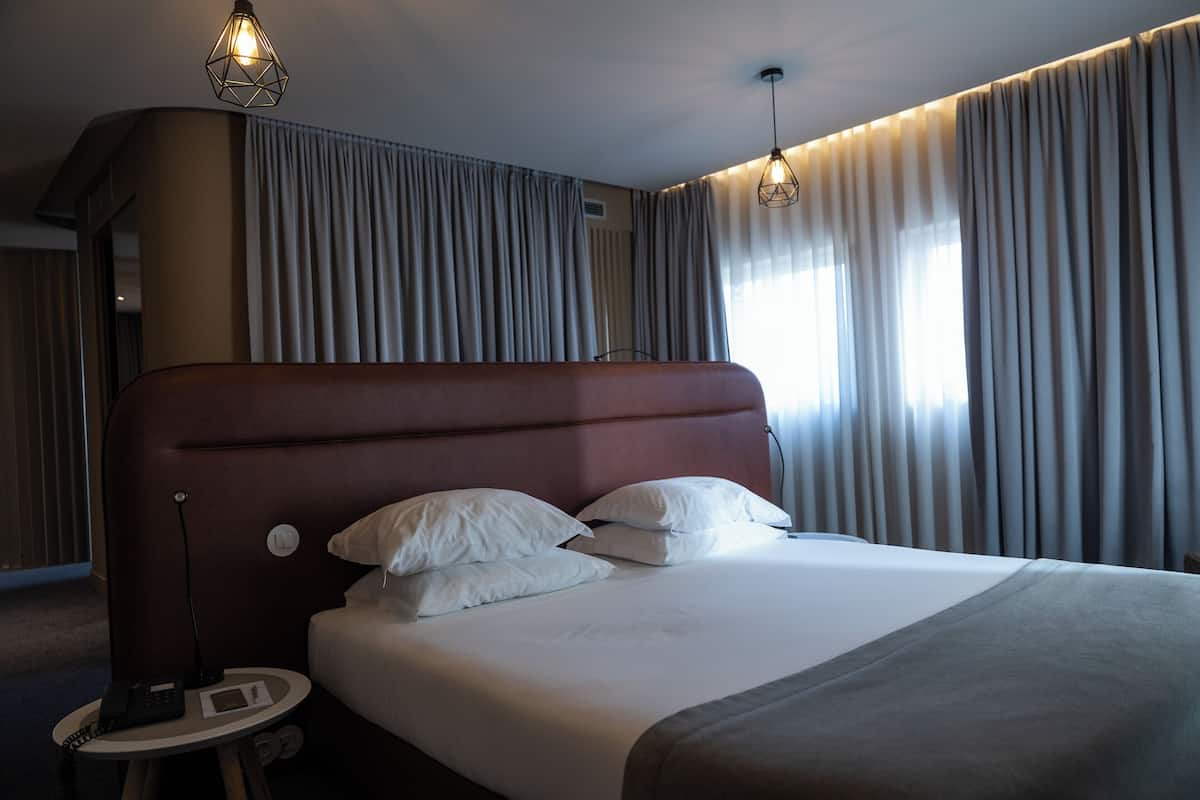 Una habitación de hotel con una cama grande, una mesita de noche con lámpara y cortinas en las ventanas.