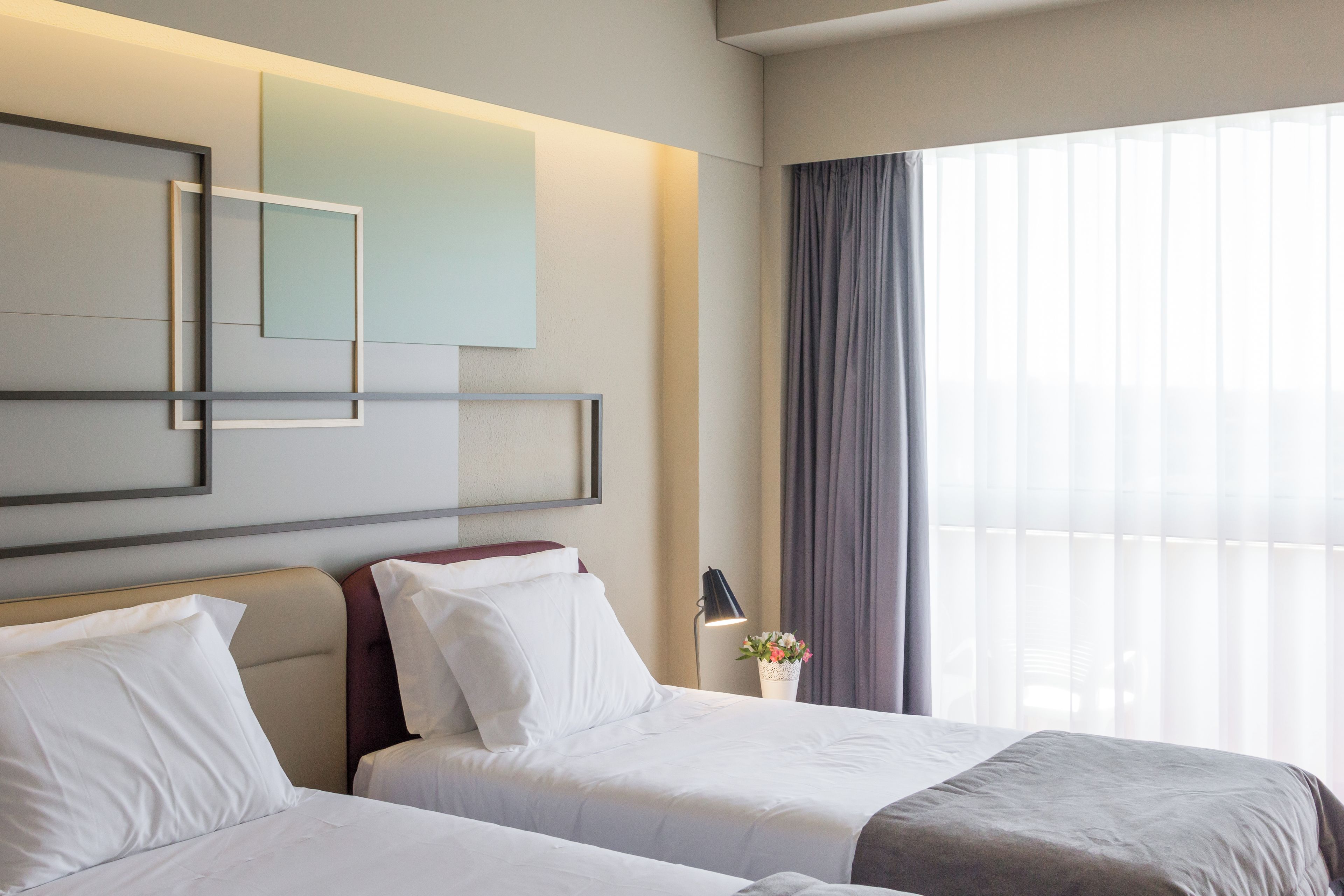 Habitación de hotel con dos camas, un ventanal con cortinas y una obra de arte colgada en la pared.