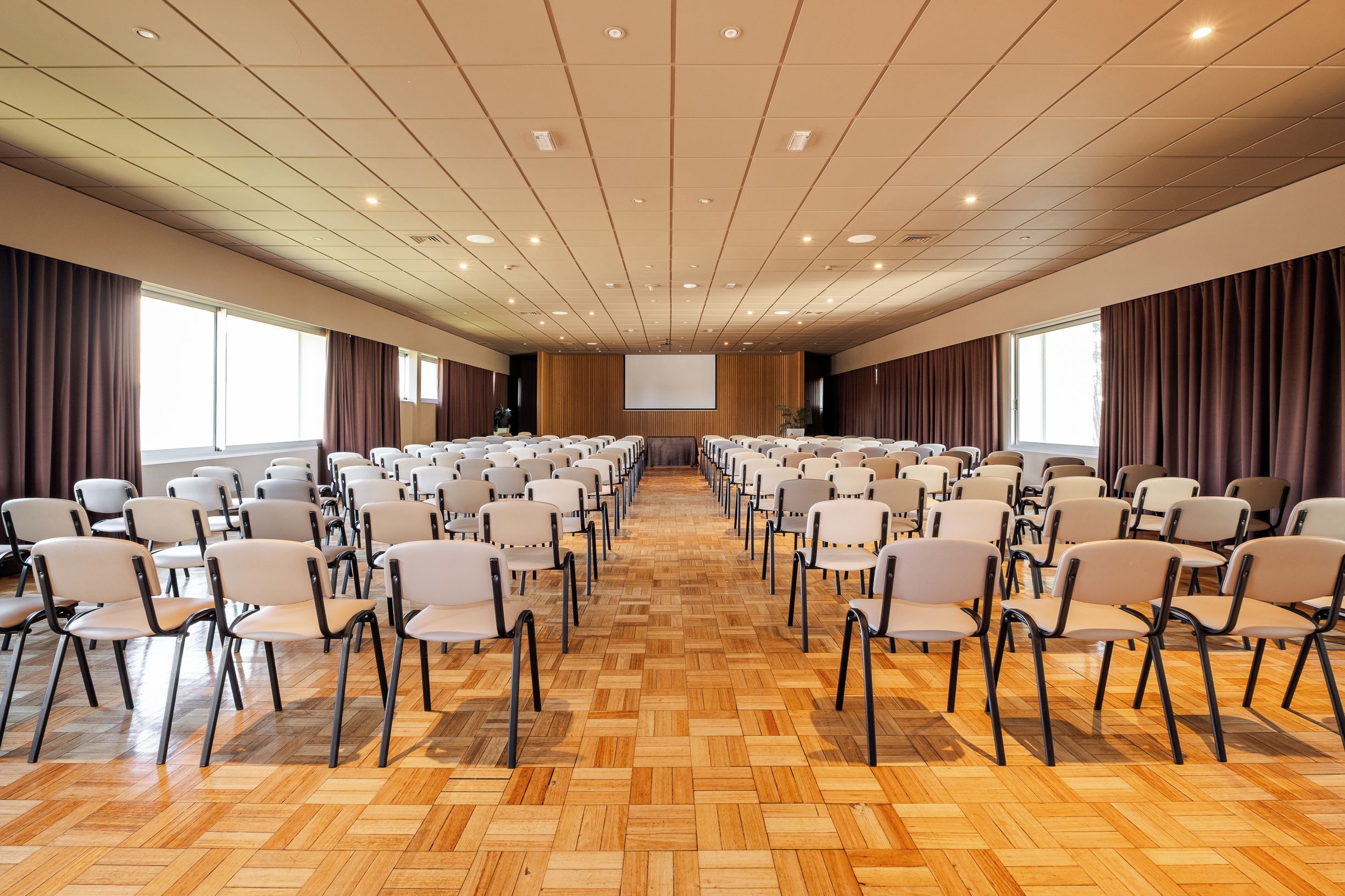 A conference room with rows of chairs, a projector screen, and large windows.