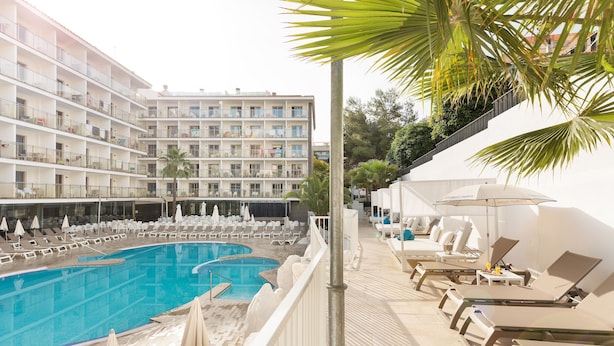 Un hotel con una piscina grande, tumbonas y un edificio de varios pisos con balcones.