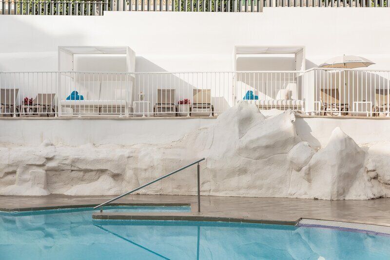 Una piscina al aire libre, sombrillas, sillones reclinables de piscina