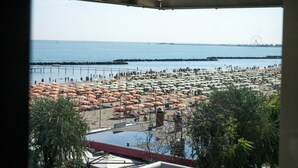 A beach view through a window with umbrellas, a pier, and a Ferris wheel in the distance. - Hotel LaMorosa (Rimini)