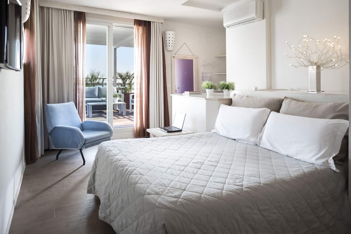 A hotel room with a large bed, a desk with a laptop, a chair, and a view of the outdoors.