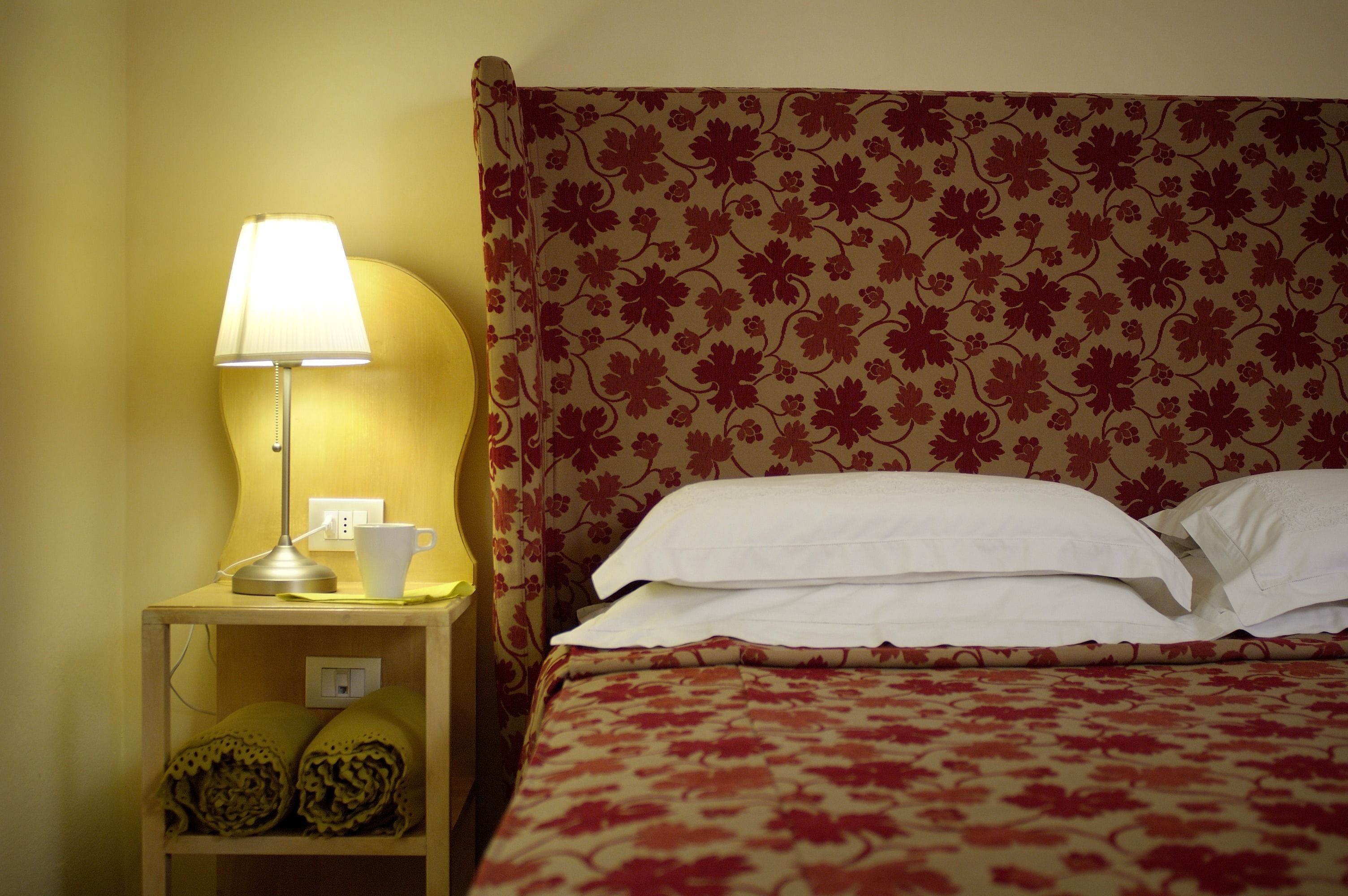 A neatly made bed with a floral-patterned headboard, a bedside lamp, and a cup on the nightstand.