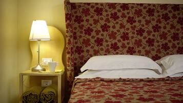 A neatly made bed with a floral-patterned headboard, a bedside lamp, and a cup on the nightstand.