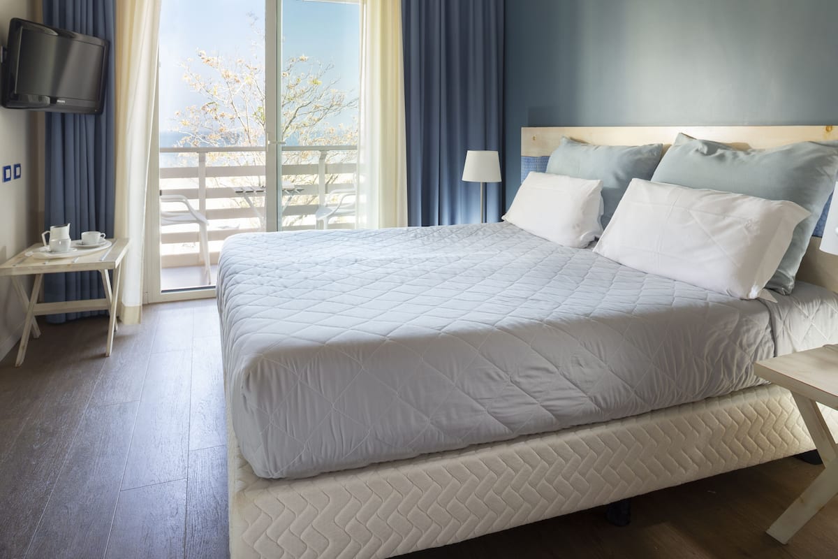 A hotel room with a large bed, a bedside table with a lamp, and a TV mounted on the wall.