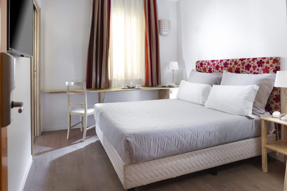 A neatly arranged hotel room with a bed, a desk, a chair, and a TV.