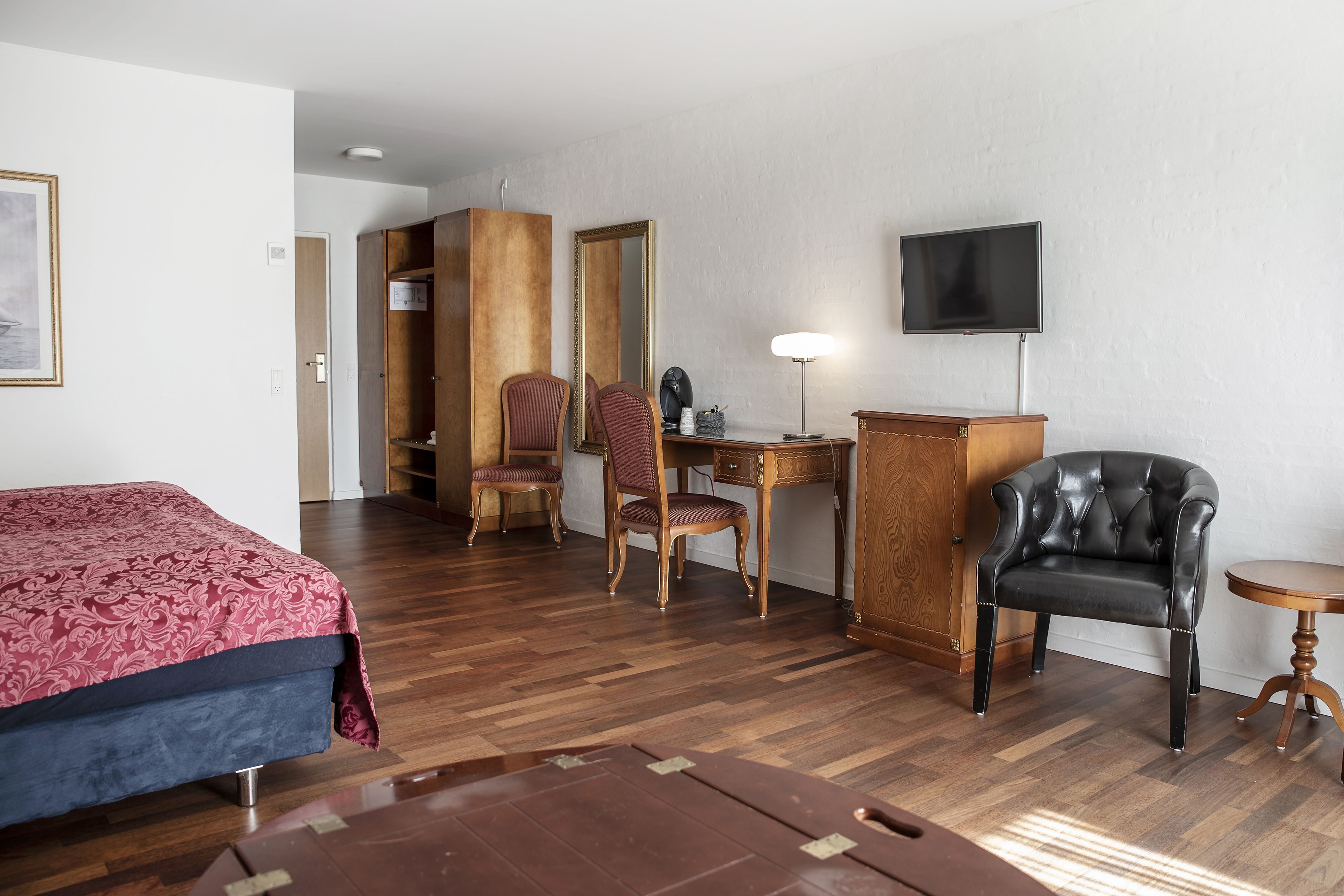 Ein Hotelzimmer mit Bett, Schreibtisch, Stuhl, Fernseher und Kleiderschrank.