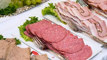 A buffet table with various meats, including sliced ham and salami, arranged on white plates with lettuce and grapes.