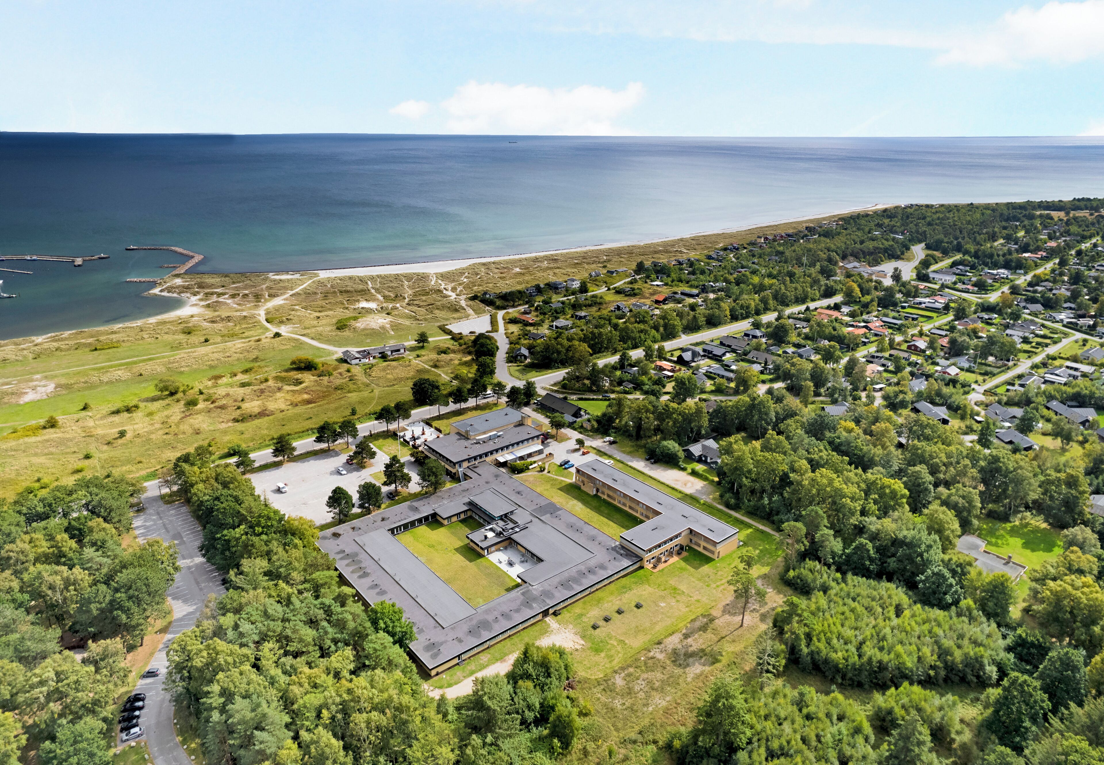 Vue aérienne d’une zone côtière comprenant un vaste complexe de bâtiments, une plage et des habitations.