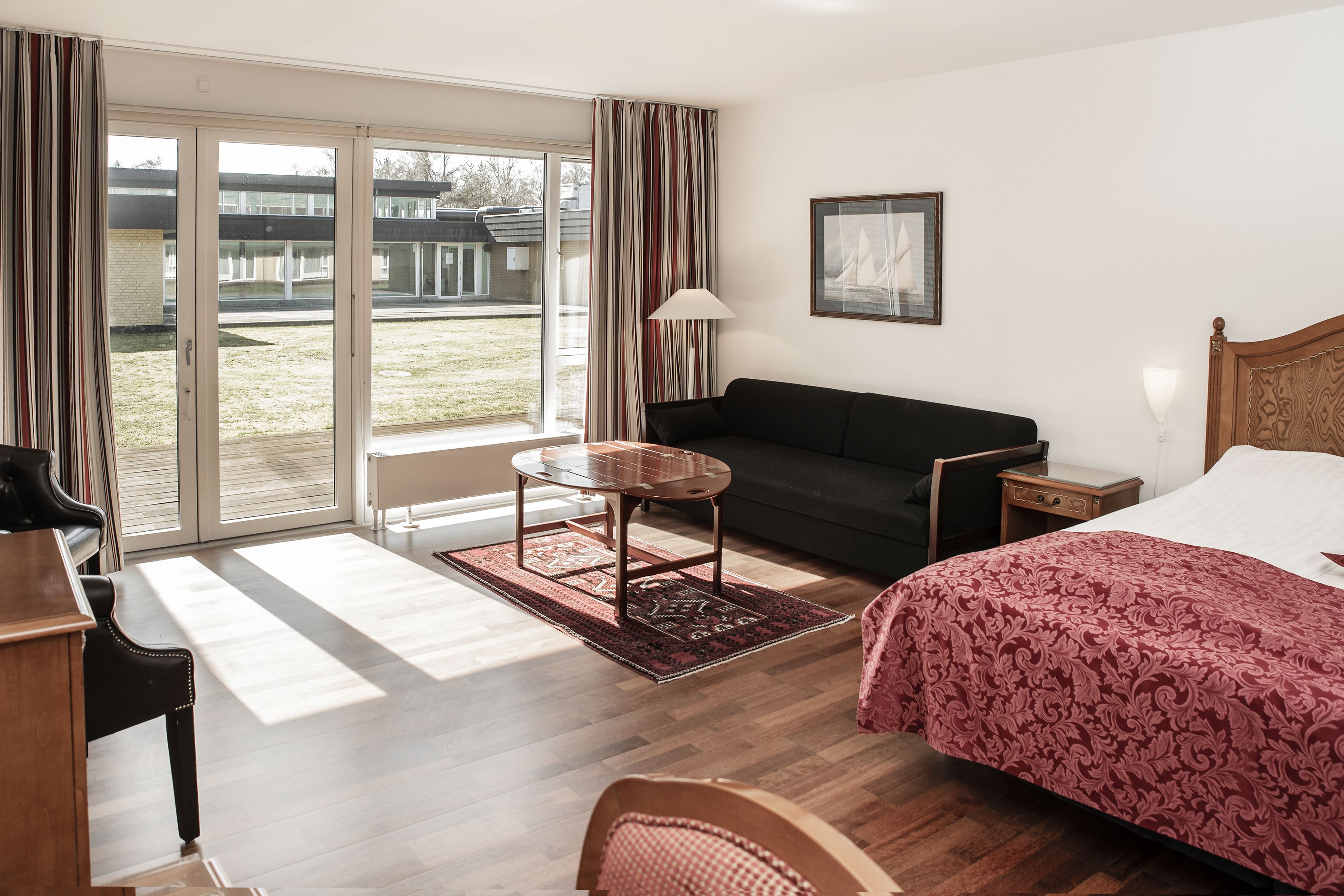 A hotel room with a bed, a sofa, a small table, a chair, and a piano.