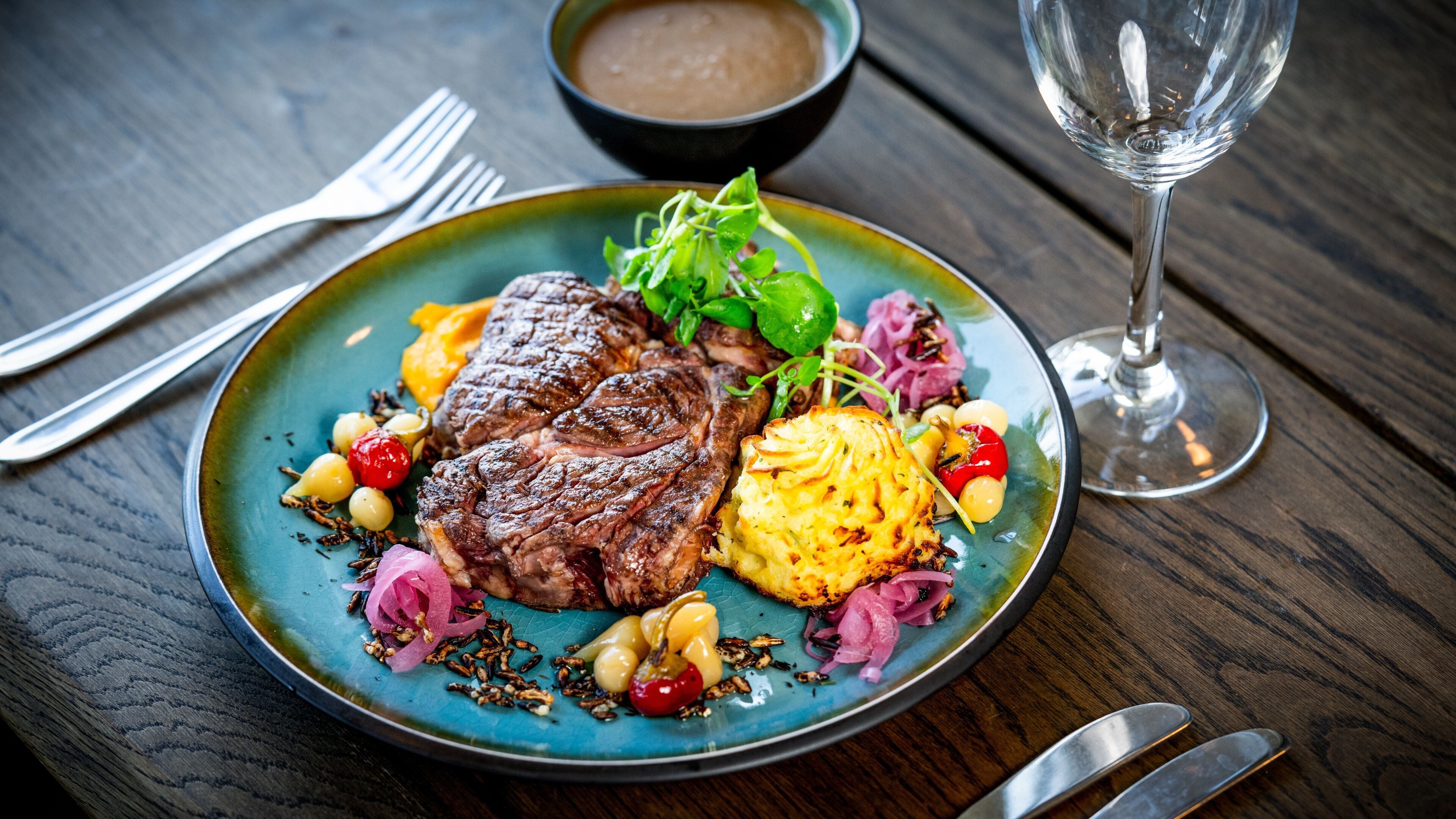 Een bord met steak, groenten en een glas wijn op een houten tafel.