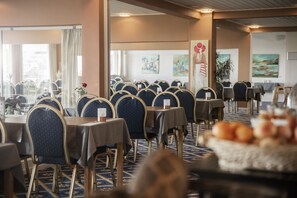 A hotel dining area with multiple tables and chairs, a buffet with fruits, and artwork on the walls. - Hotel Marina (Grenaa)