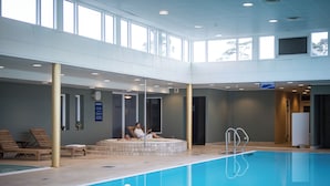 Une piscine intérieure avec un atrium baigné de lumière naturelle, des chaises longues et un espace dédié aux soins.