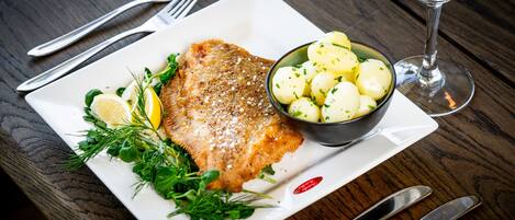 Un plato de pescado con limón y hierbas, un bol de patatas y un vaso de agua sobre una mesa de madera.