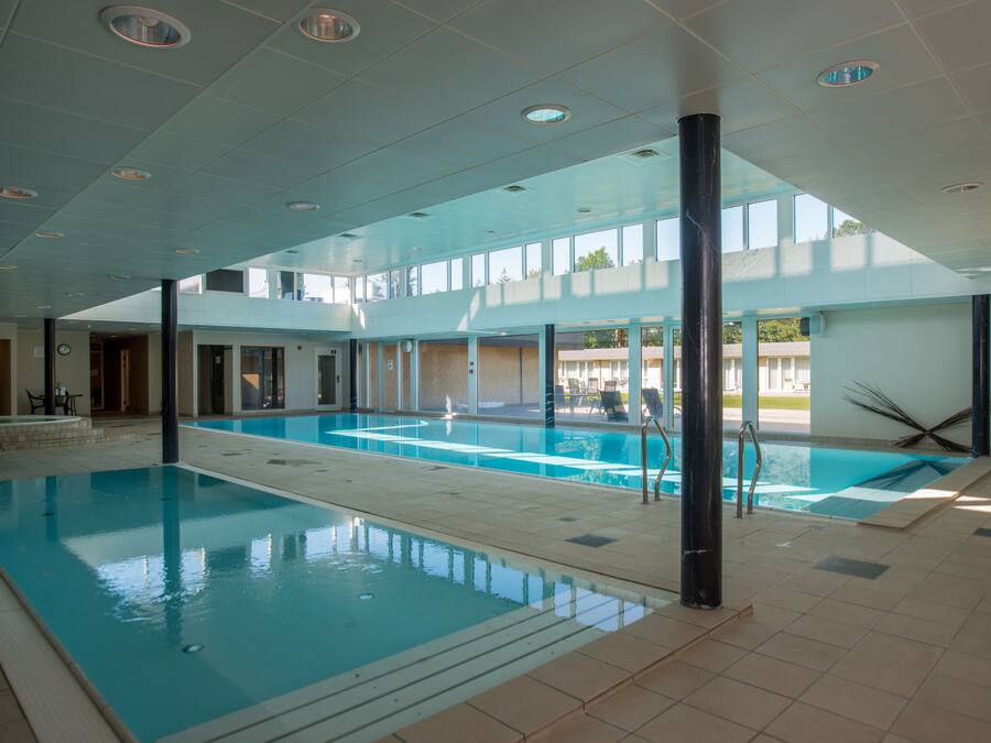 Une piscine intérieure à l’eau d’un bleu limpide, entourée de murs et de sols recouverts de carreaux, et dotée de grandes fenêtres qui laissent entrer la lumière naturelle.