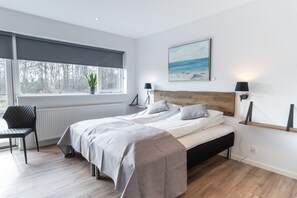 A modern bedroom with a large bed, a chair, a window with a view of trees, and a painting on the wall. - Hotel Marina (Grenaa)