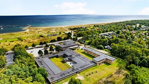 Une vue aérienne d’un vaste complexe immobilier composé de plusieurs bâtiments, entouré de verdure et bordé par une plage.