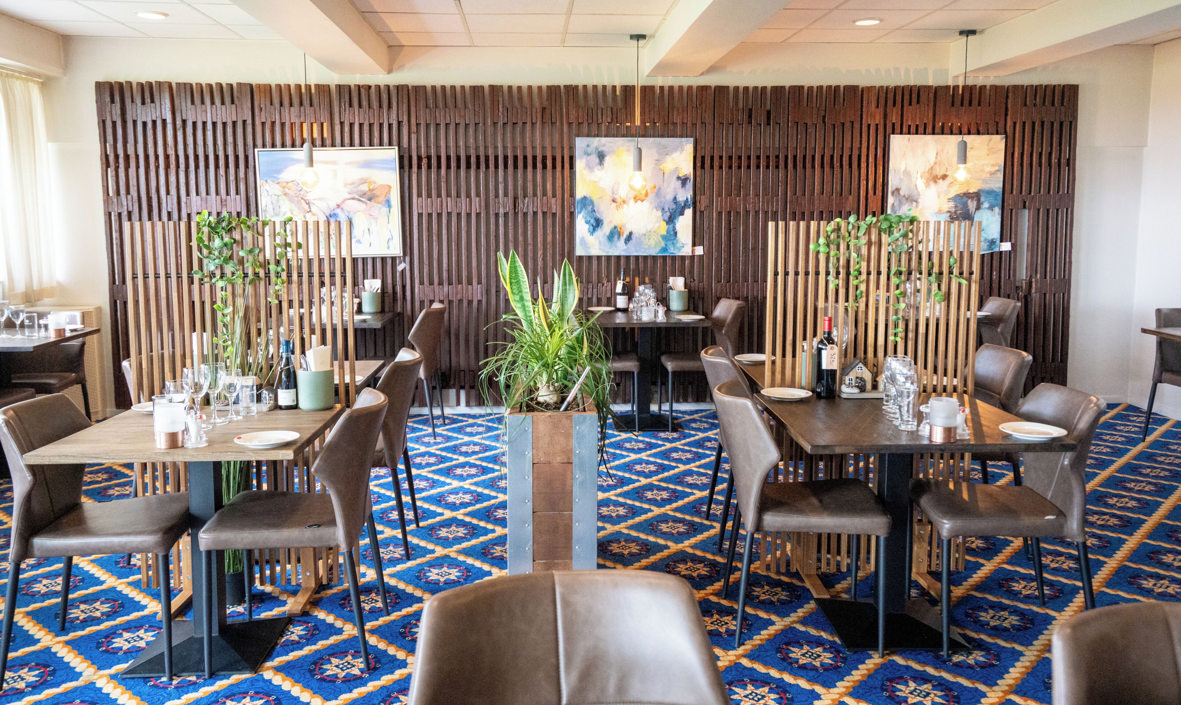 Un restaurant amb parets revestides de fusta, un sòl de moqueta amb dibuixos blaus i diverses taules amb cadires.