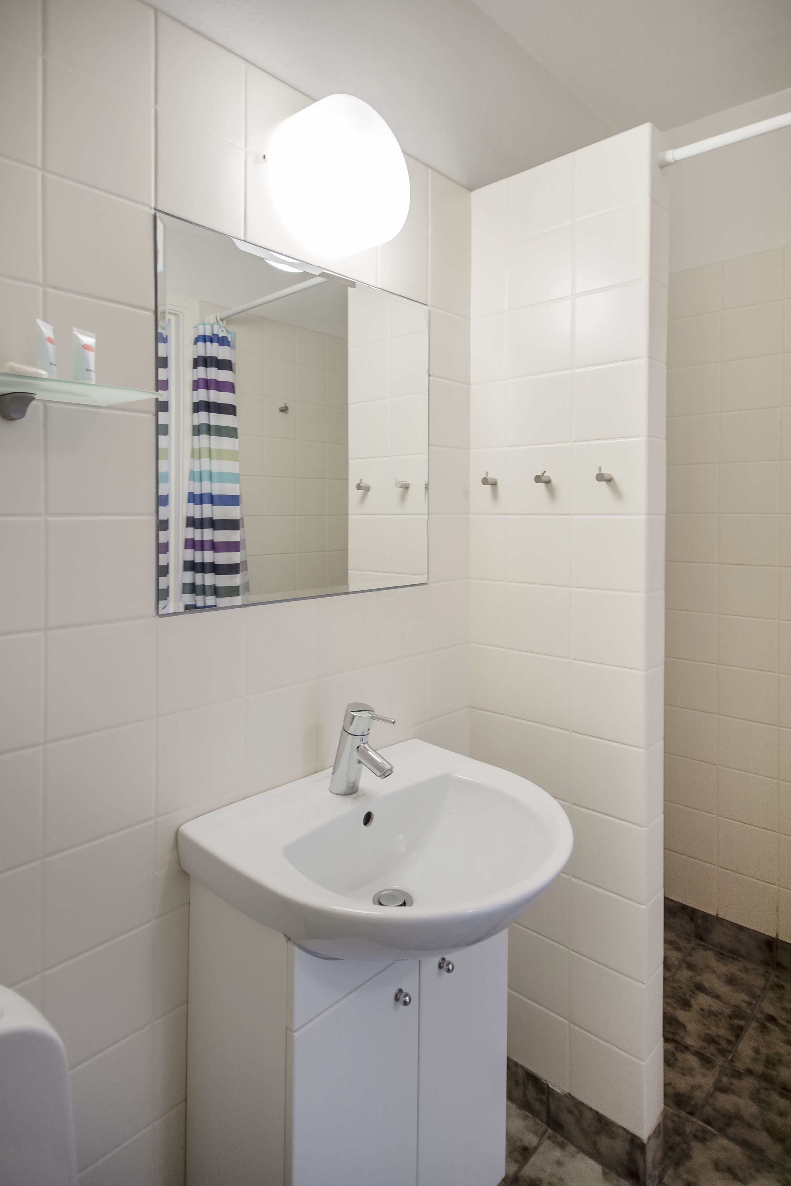 Een badkamer met witte tegels, een witte wastafel, een spiegel en een douchehoek.