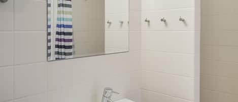 A bathroom with white tiles, a white sink, a mirror, and a shower area.