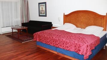 A bedroom with a wooden bed, a black sofa, a small table, and a window with curtains.